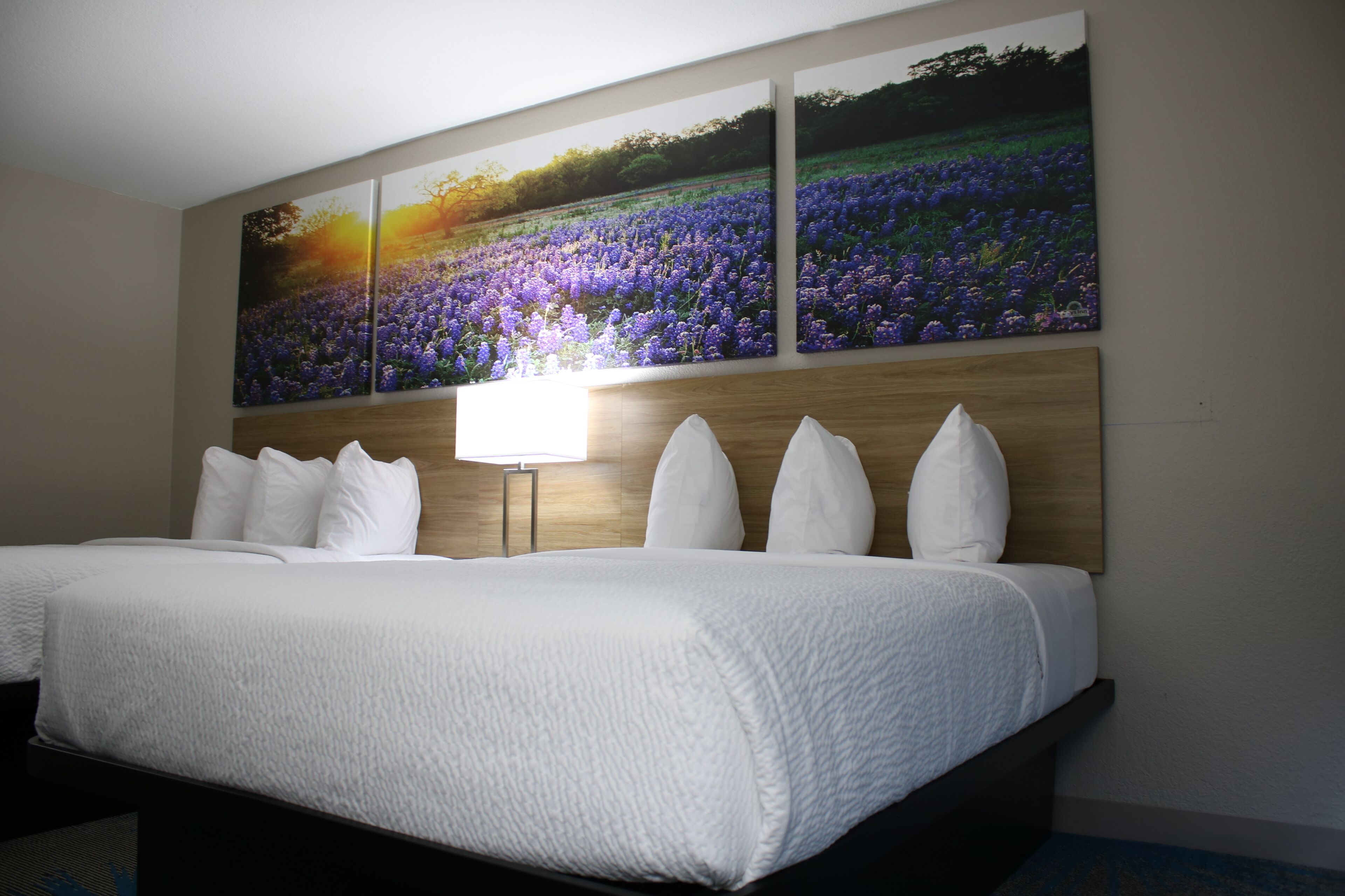 Et hotelværelse med en stor seng, et træhovedgærde og et ophængt maleri af lilla blomster.