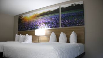 A hotel room with a large bed, a wooden headboard, and a wall-mounted painting of purple flowers.