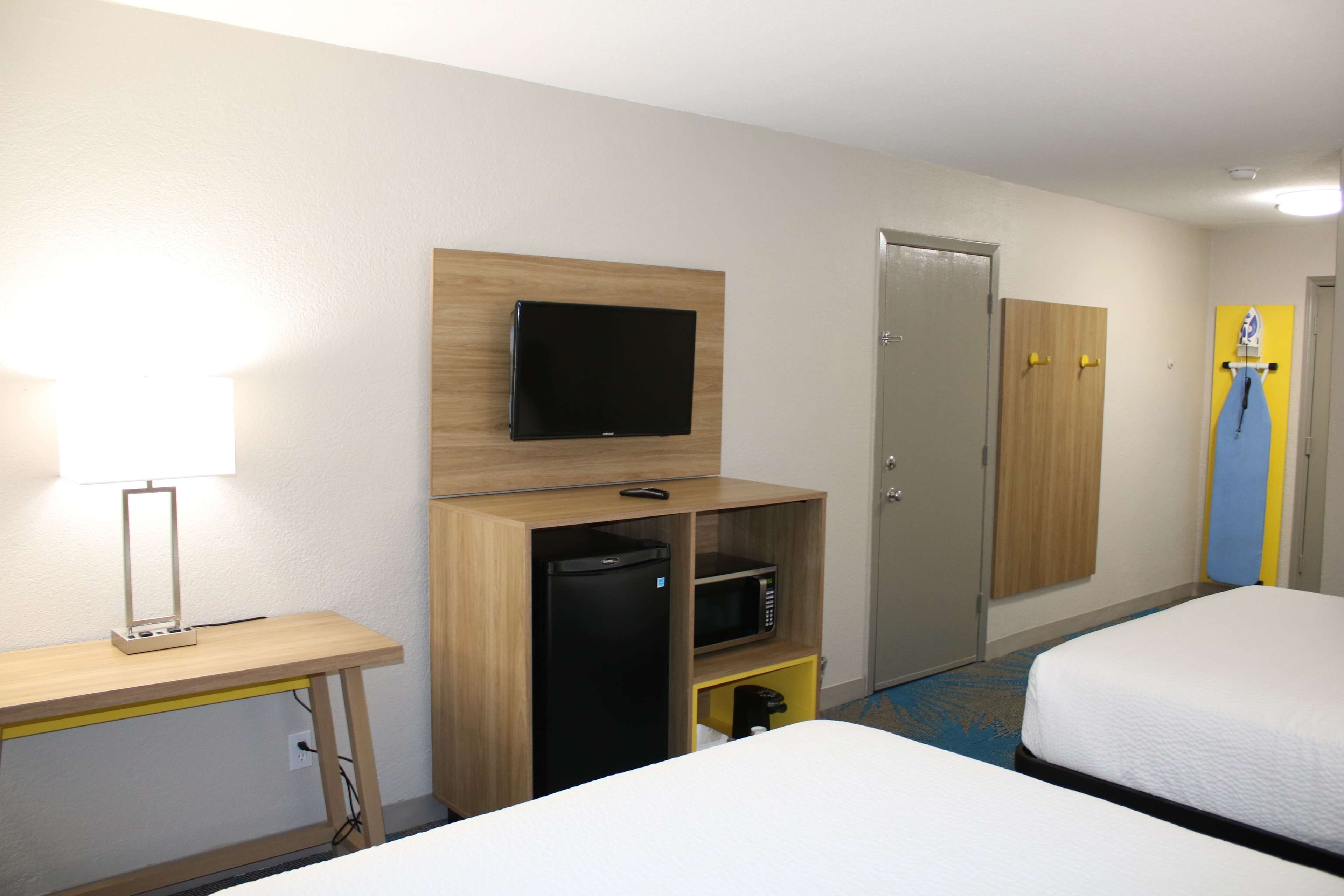 Une chambre d’hôtel comprenant un lit, un bureau avec une lampe, une télévision, un four à micro-ondes et une armoire.