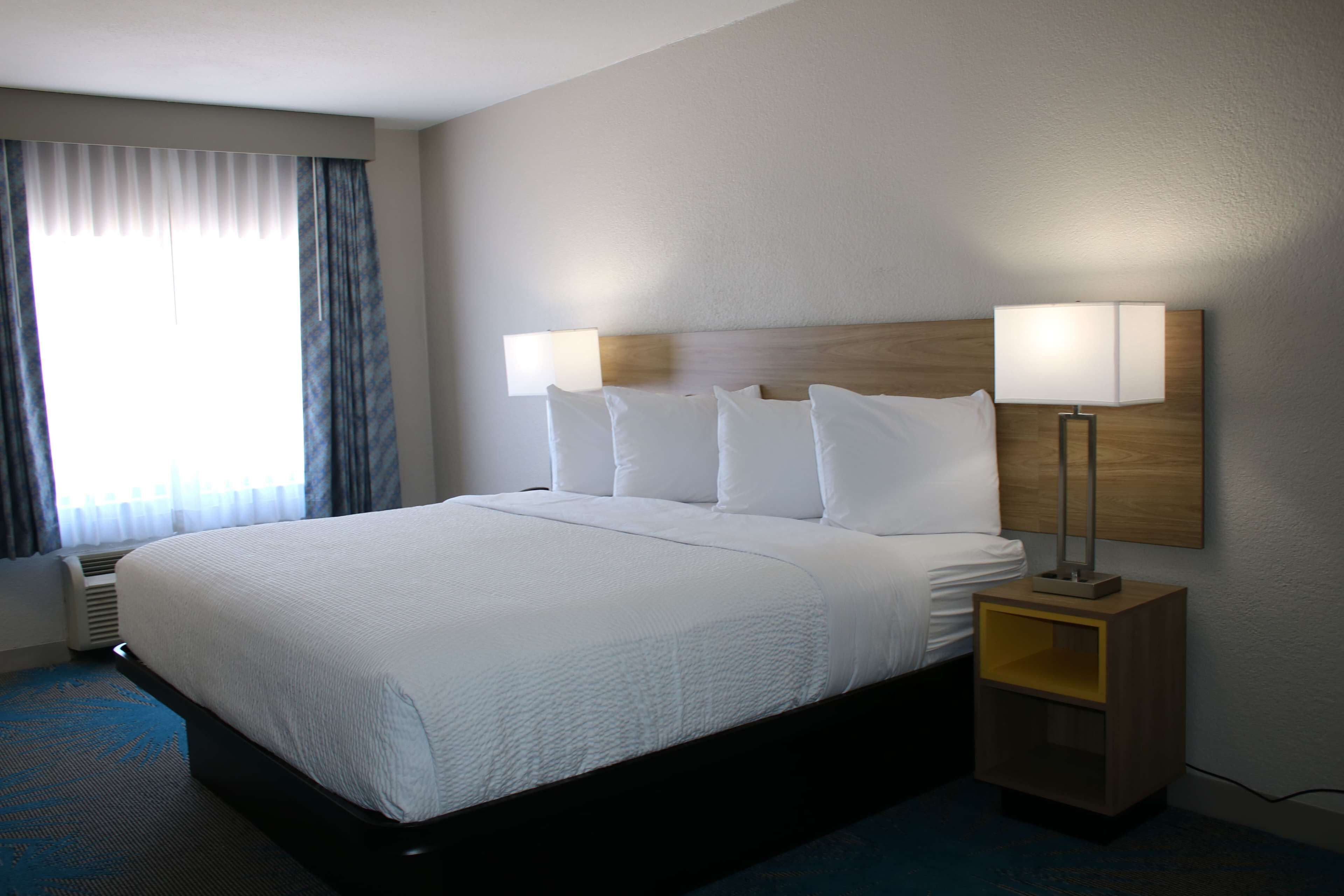 Ein Hotelzimmer mit einem großen Bett, zwei Nachttischlampen und einem Fenster mit Vorhängen.