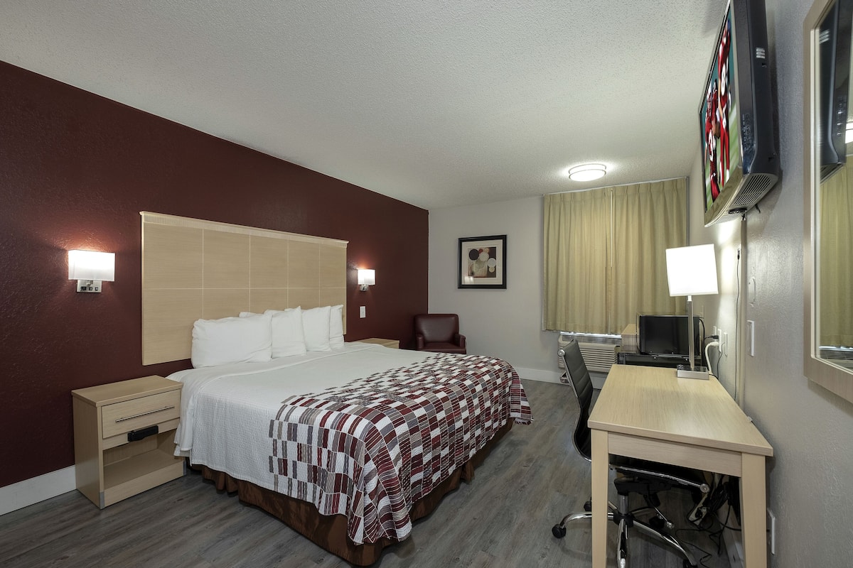 A hotel room with a bed, bedside tables, a desk, a chair, a TV, and a window with curtains.