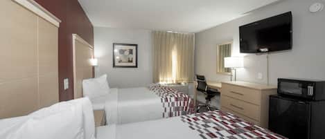 A hotel room with two beds, a desk, a chair, a TV, a microwave, and a picture on the wall.