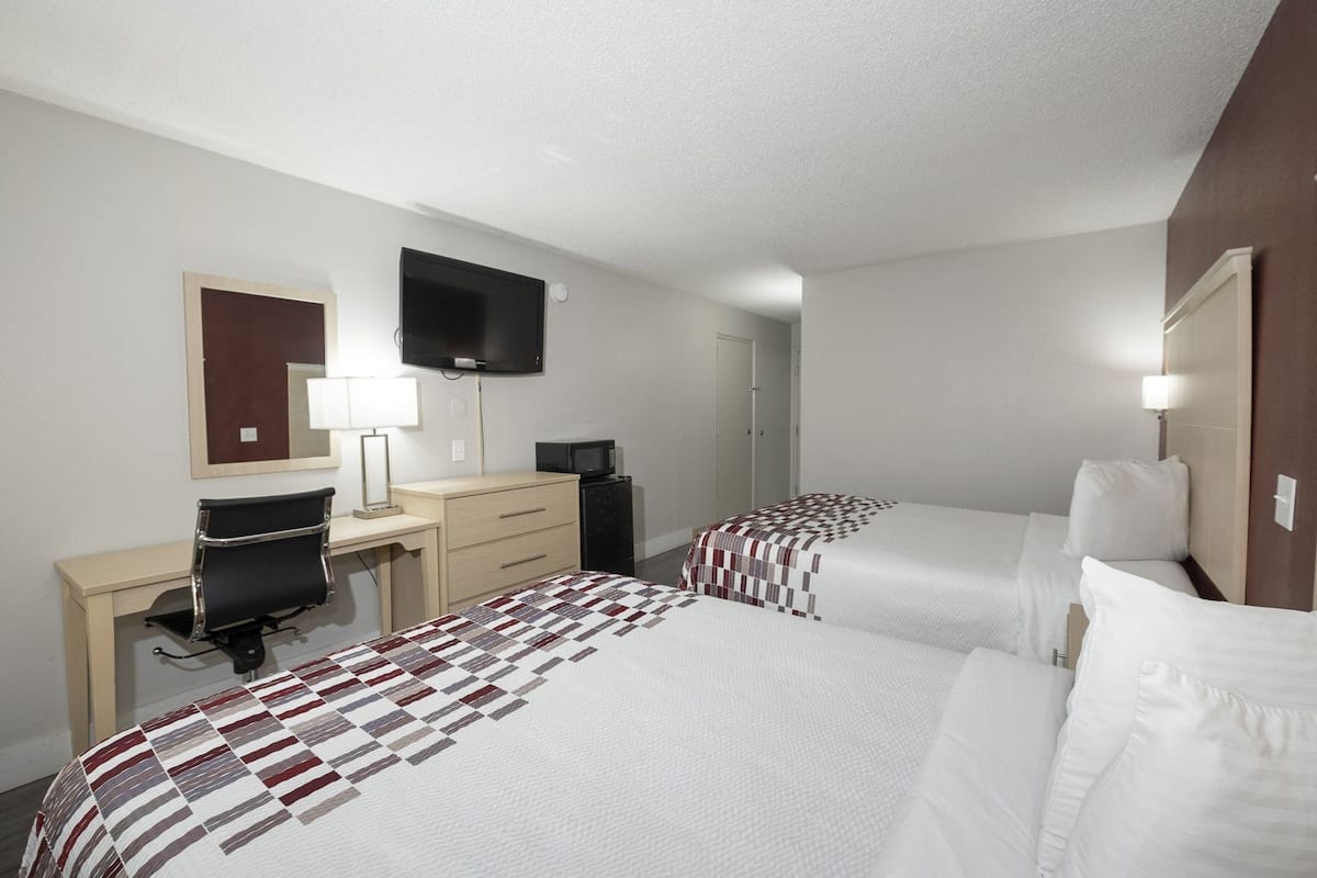A hotel room with two beds, a desk, a chair, a TV, and a mirror.