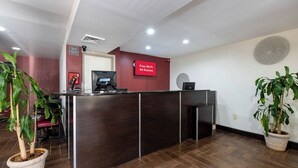 A reception desk with a digital screen, a 'Free Wi-Fi All Rooms' sign, and a potted plant. - Red Roof Inn Raleigh North-Crabtree Mall/Lenovo Center (Raleigh)