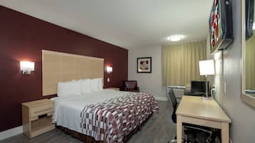 A hotel room with a bed, bedside tables, a desk, a chair, a television, and a window with curtains.