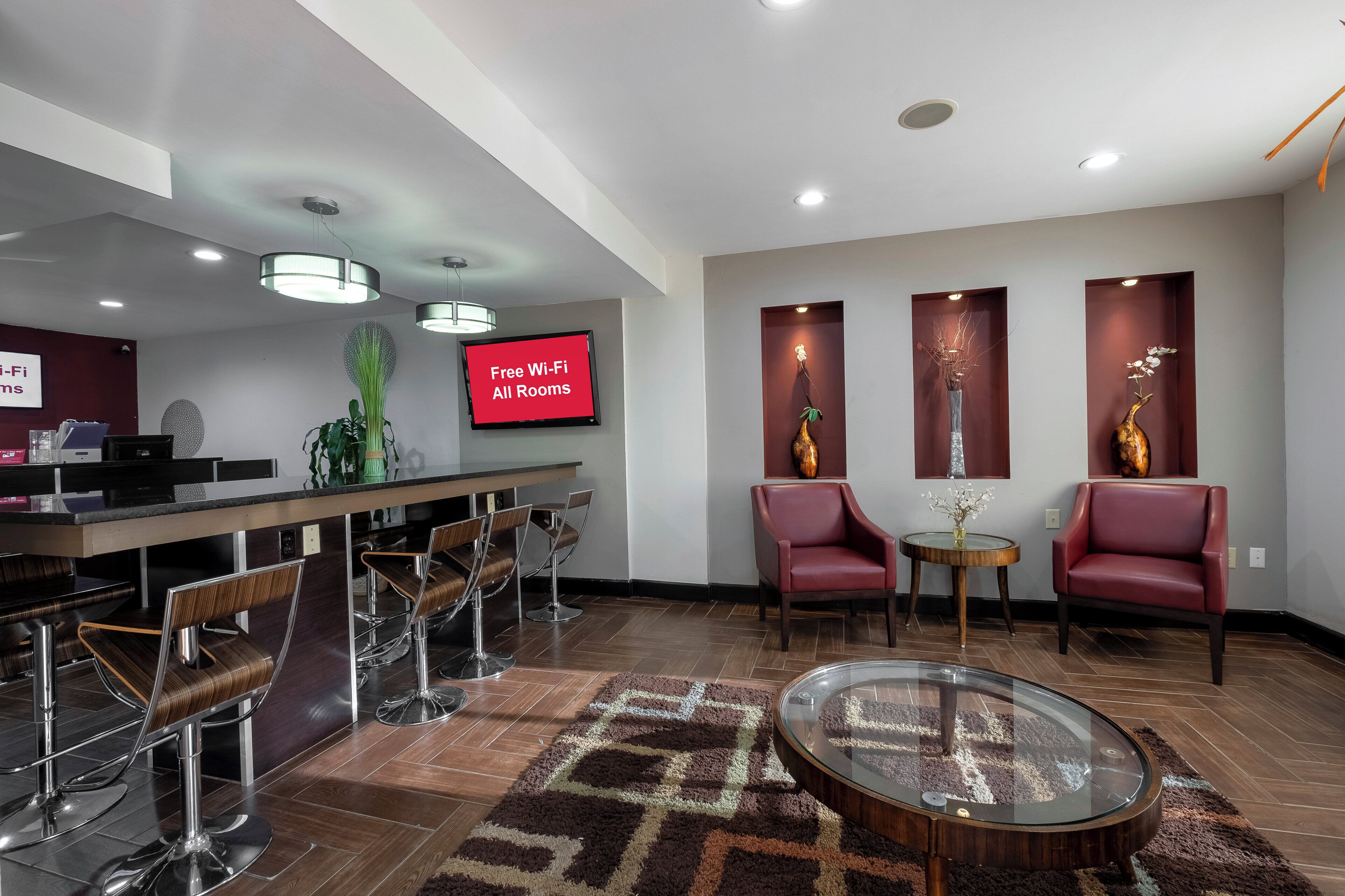 A hotel lobby with a reception desk, bar area, seating, and a TV displaying 'Free Wi-Fi All Rooms'.