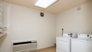 A laundry room with a wall-mounted heater, a vent, and stacked washing machines. - Red Roof Inn Raleigh North-Crabtree Mall/Lenovo Center (Raleigh)