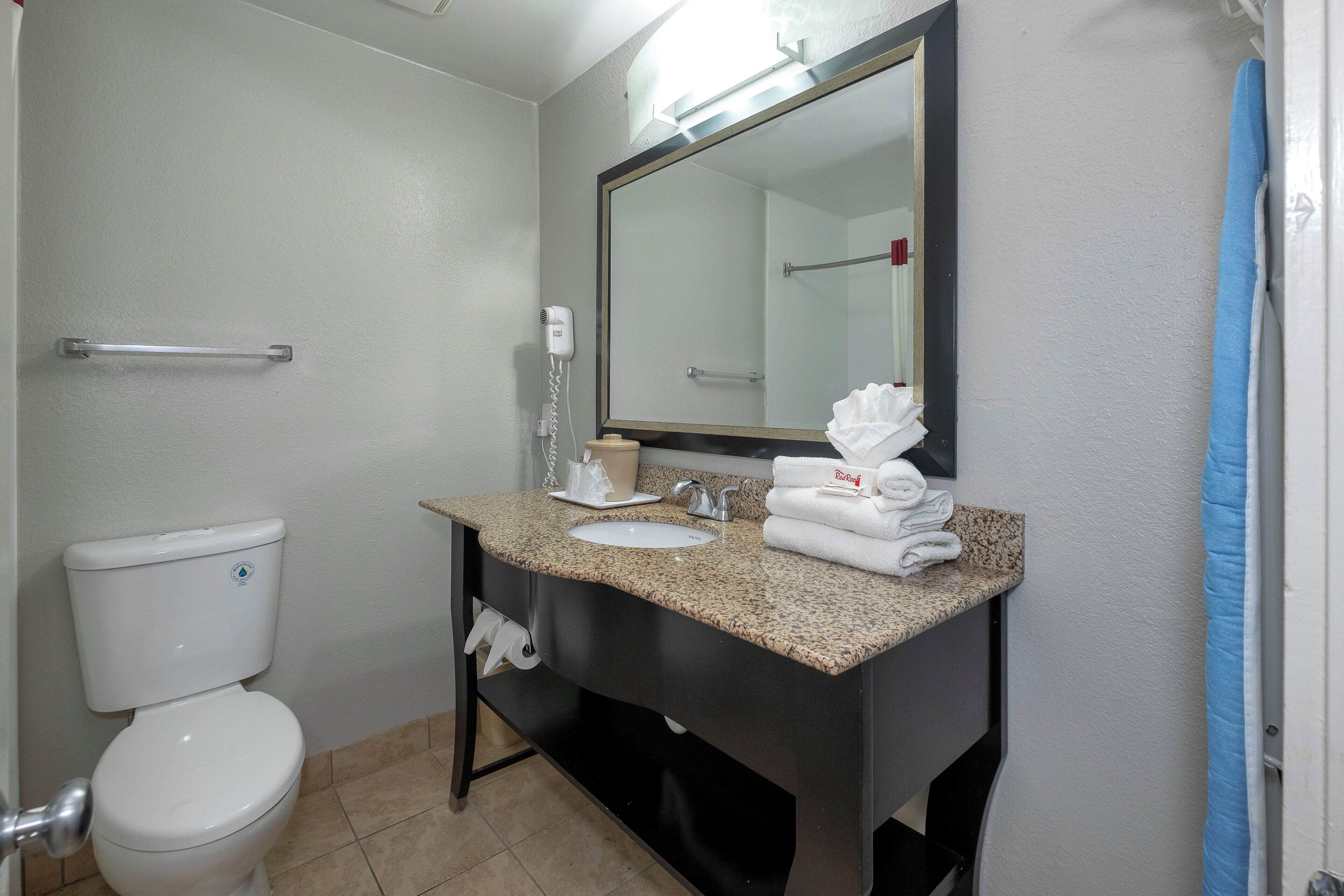 Une salle de bain équipée de toilettes, d’un lavabo, d’un miroir, d’un porte-serviettes et d’un sèche-cheveux.