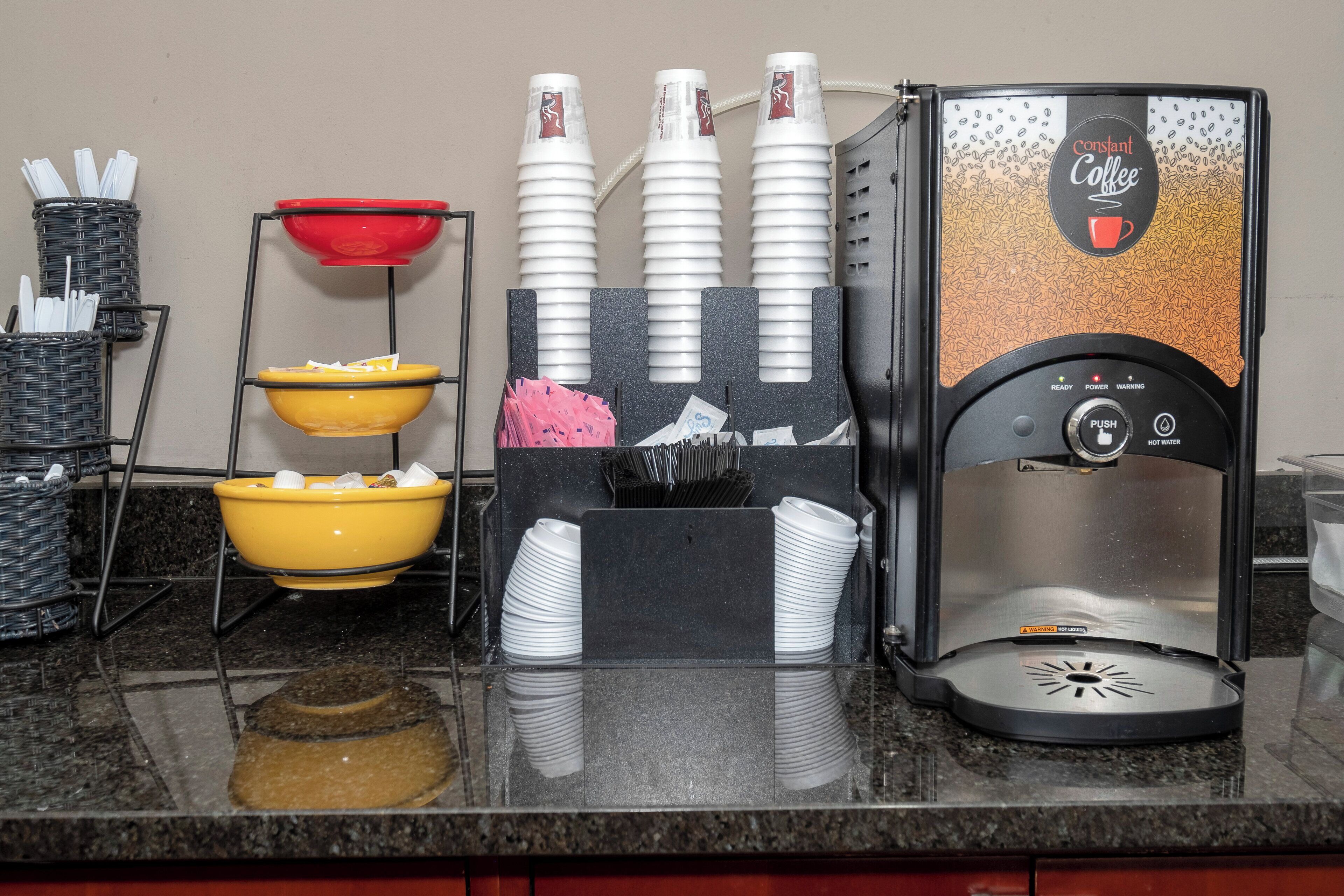 A coffee station with a coffee machine, cups, and a bowl of fruit.