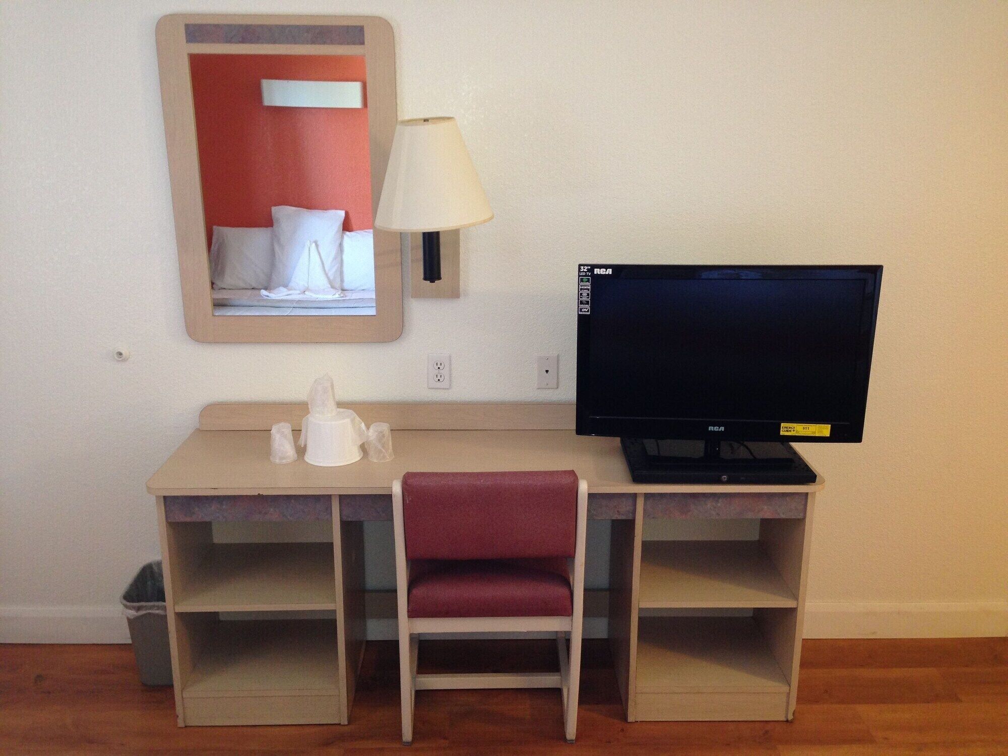 A small hotel room with a desk, chair, television, and a mirror.