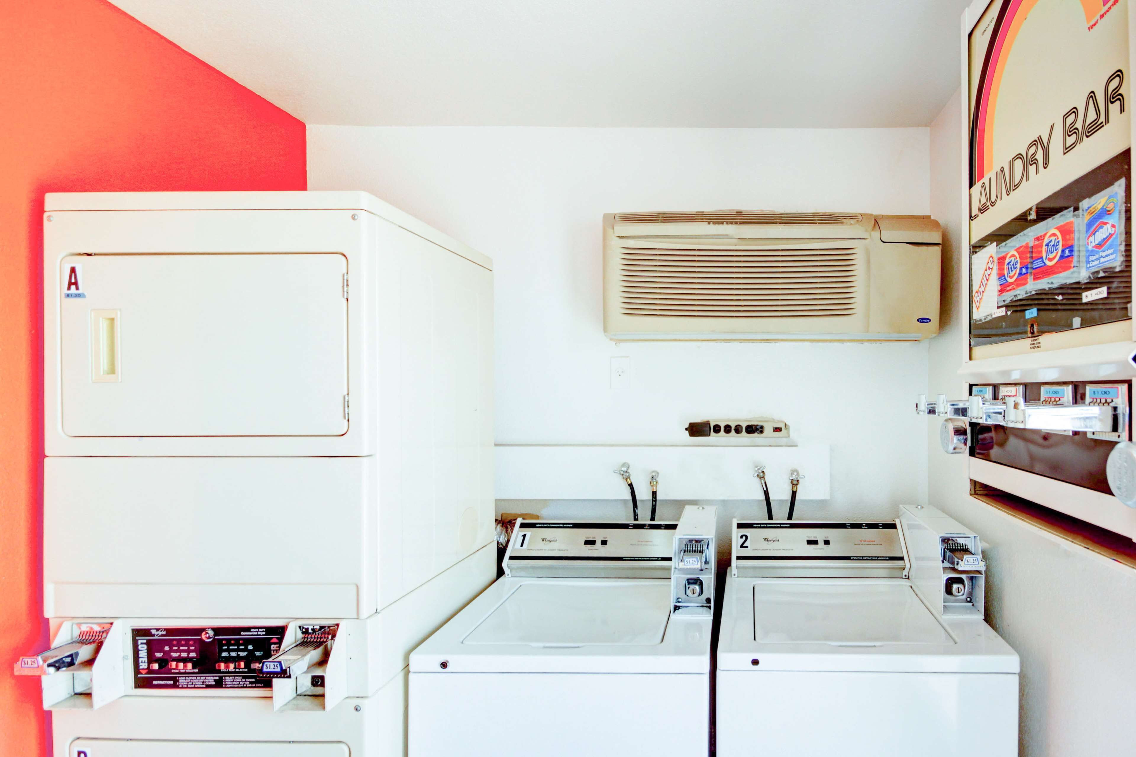 A laundry room with two dryers, a washing machine, and a wall-mounted air conditioner.