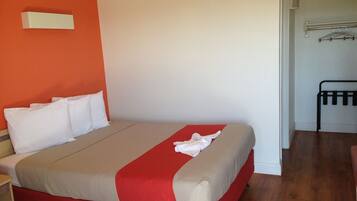 Una habitación de hotel con una cama, una colcha roja y beige, almohadas blancas y suelo de madera.