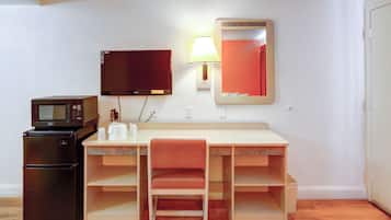 Habitación compacta con kitchenette, escritorio y silla, televisor de pantalla plana, lámpara y espejo.