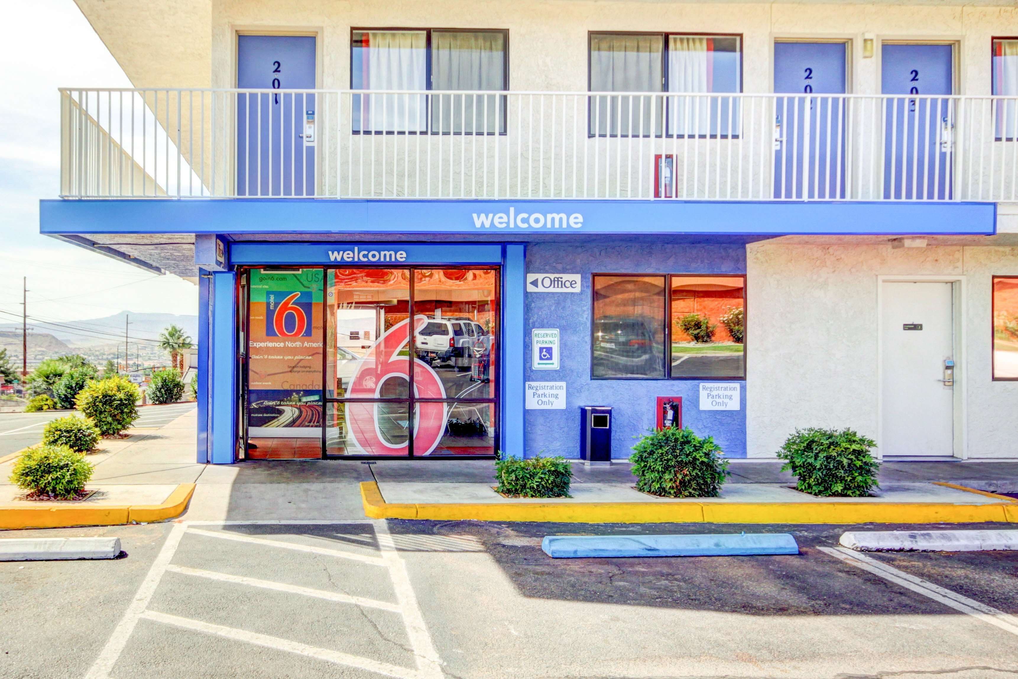Entrada de hotel con toldo azul, un letrero de 'Welcome' y un cartel con el número '6'.