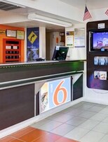 Zona de recepción de un hotel con mostrador, pantalla digital y bandera estadounidense.