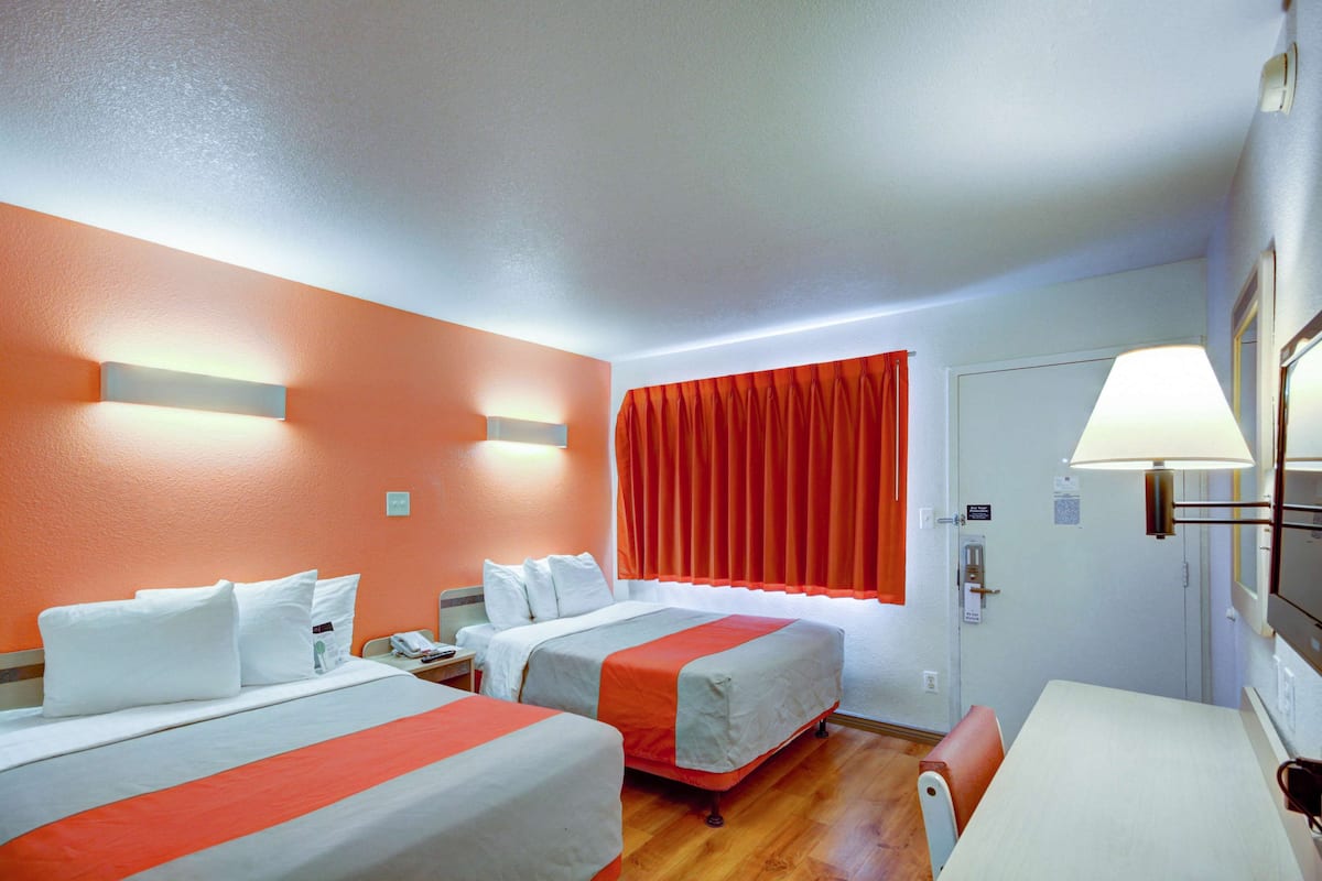 A hotel room with two beds, a desk, and a chair.