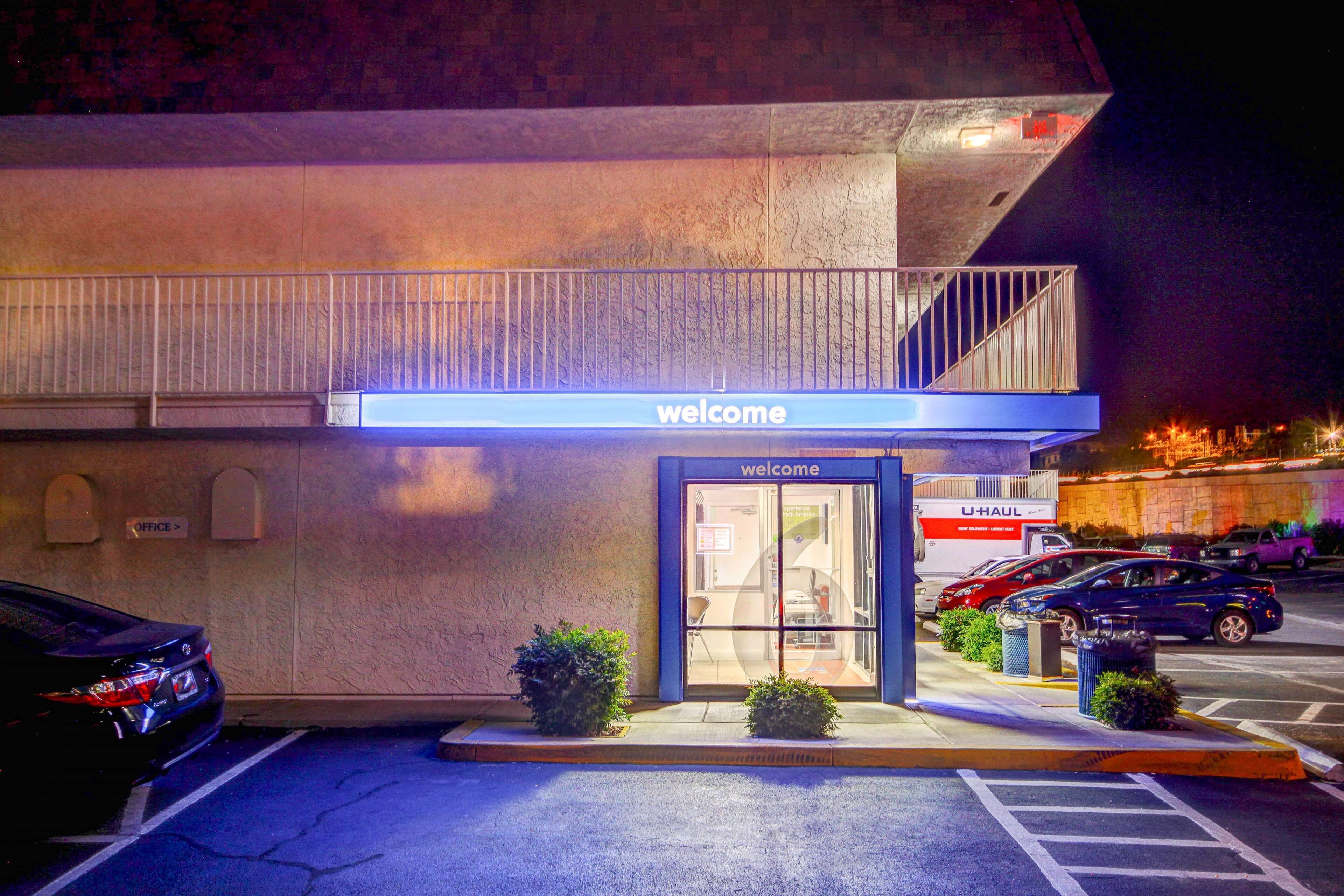 A U-Haul rental office at night with a 'Welcome' sign above the entrance, a parking lot, and a building with a balcony.
