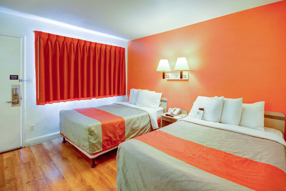 A hotel room with two beds, a red curtain, a nightstand with a lamp, and a phone.