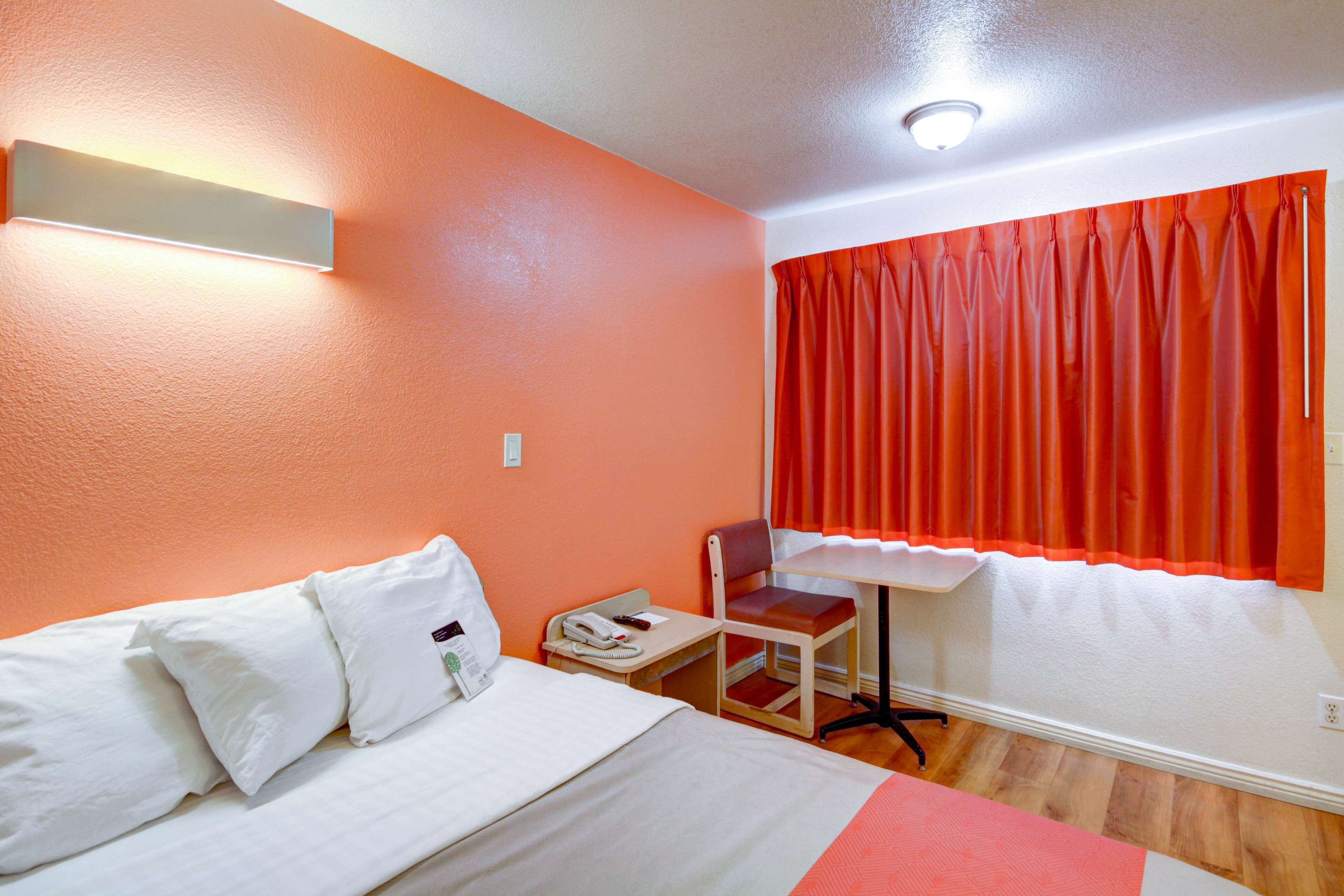 Quarto de hotel com uma cama, uma escrivaninha, uma cadeira e um telefone.