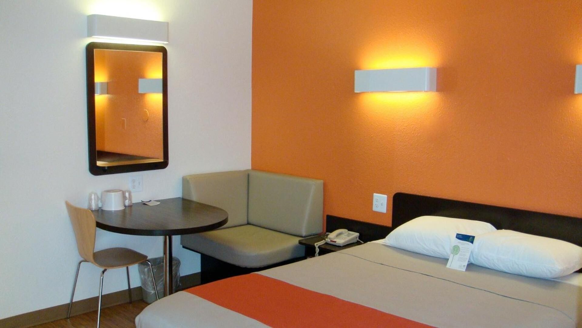 Een hotelkamer met een bed, een bureau, een stoel en een nachtkastje met een telefoon.