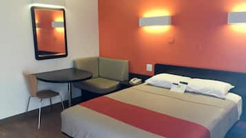 Una habitación de hotel con cama, escritorio, silla y espejo.