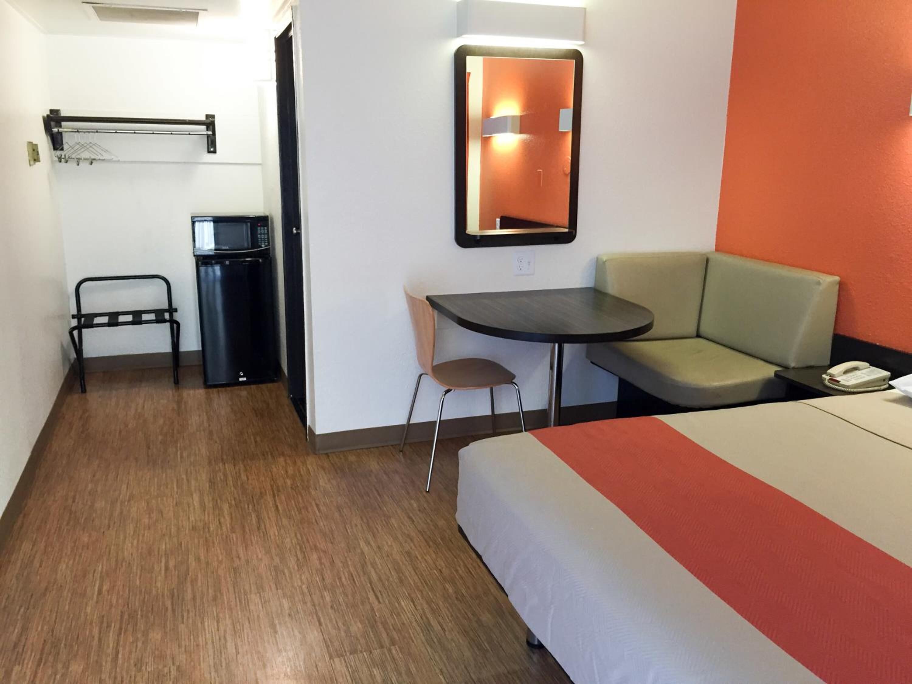A hotel room with a bed, a desk with a chair, a small table, a sofa, and a microwave.