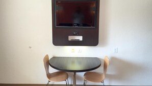 A room with a wall-mounted flat-screen TV, a small table, and two chairs. - Motel 6 Oroville, CA (Oroville)