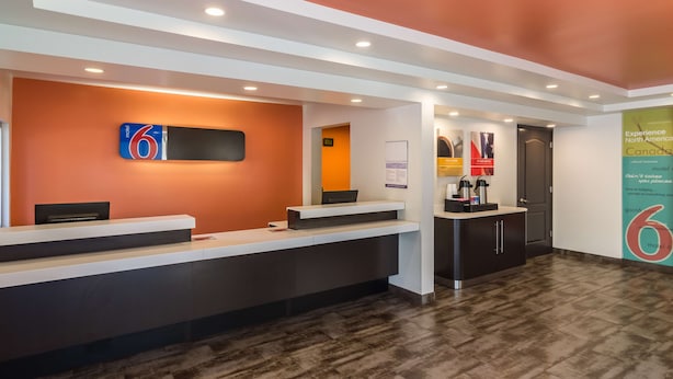 A modern hotel reception area with a reception desk, a digital screen, and a wall-mounted sign. - Motel 6 Oroville, CA (Oroville)