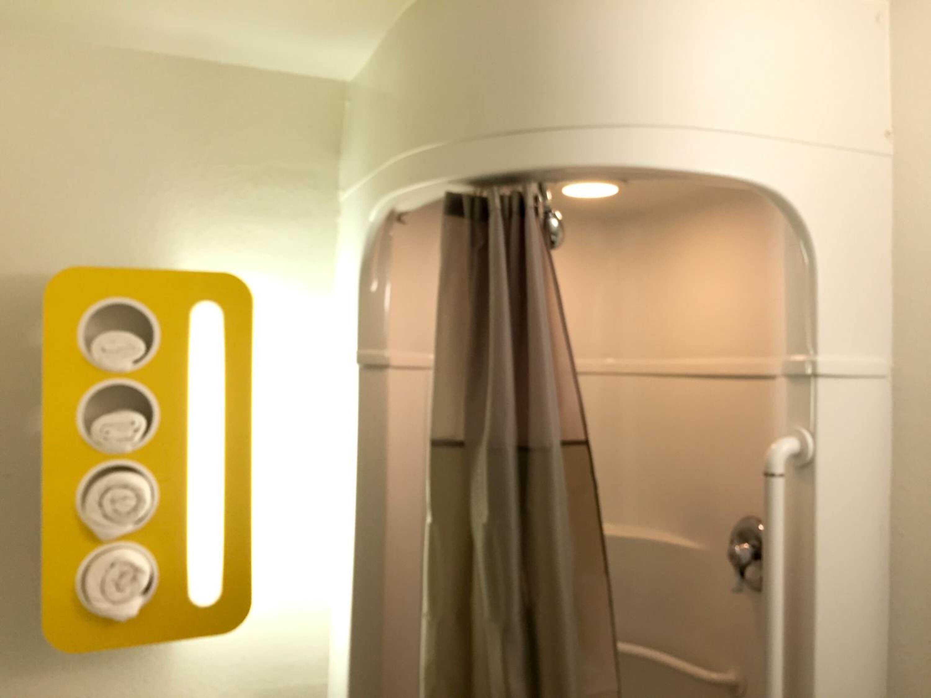 A bathroom with a shower, a yellow light switch panel, and a white wall.