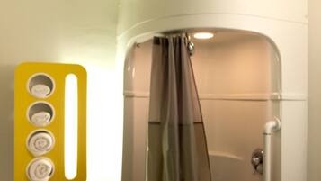 A bathroom with a shower, a yellow light switch panel, and a white wall.