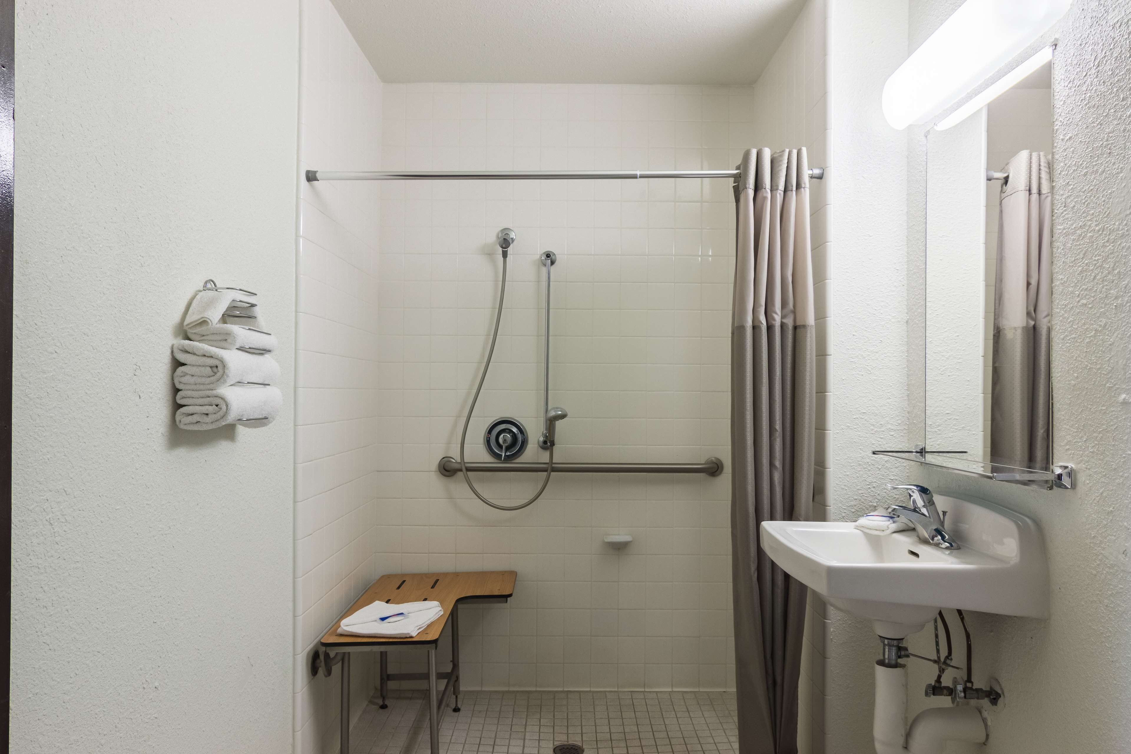 Un baño pequeño y limpio con ducha, lavamanos, espejo y toallero.