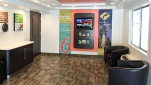 A modern hotel lobby with a reception desk, a digital screen displaying a news channel, and a large wall with promotional banners. - Motel 6 Oroville, CA (Oroville)