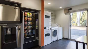 A self-service laundry area with a vending machine, washing machine, and dryer.