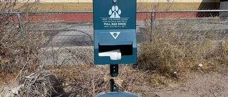 A pet waste station with a sign warning about disease transmission, a trash bin, and a fenced area.