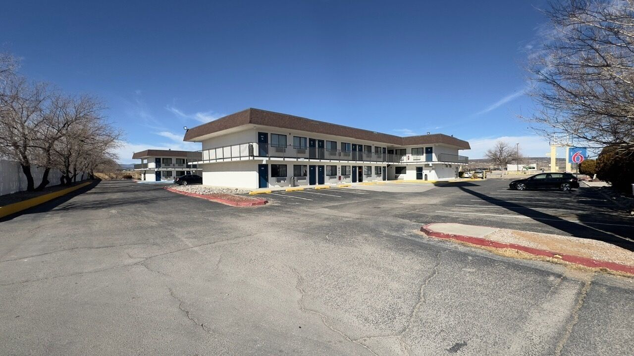 A two-story motel with a parking lot in front, a clear blue sky, and a sign indicating a nearby location.