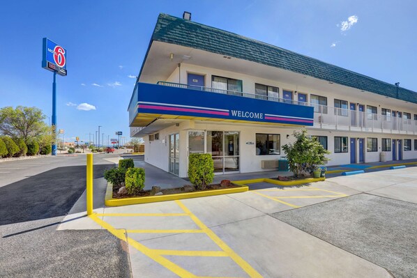 A motel with a 'Welcome' sign, a parking lot, and a clear blue sky. - Motel 6 Grants, NM (Grants)