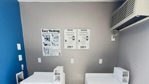 A laundry room with two front-loading washing machines, a ceiling light, and two informational posters on the wall. - Motel 6 Grants, NM (Grants)