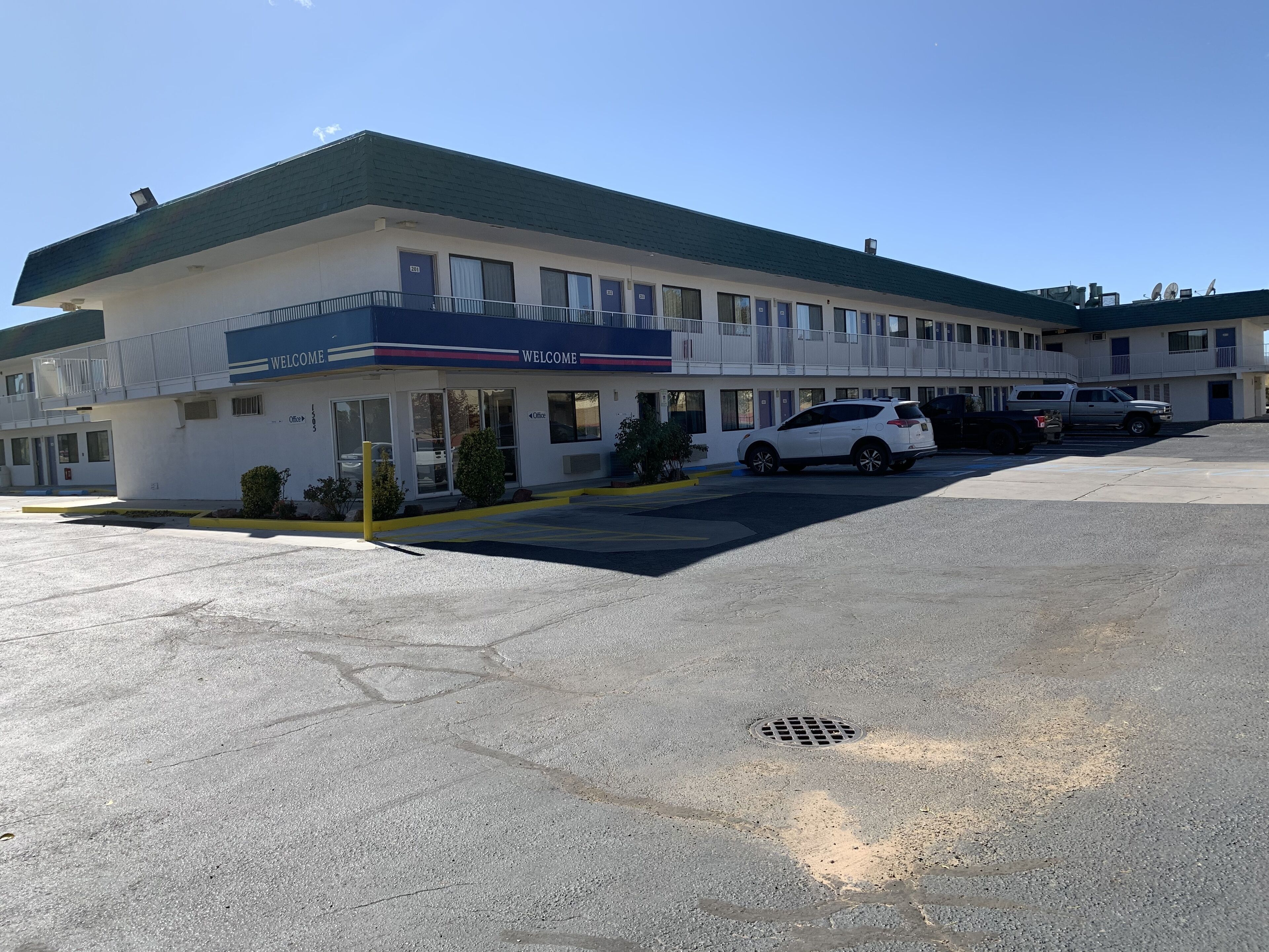 Un motel con una estructura de dos pisos, un estacionamiento y un coche blanco estacionado al frente.