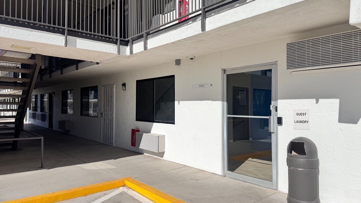 A building with a white exterior, a glass door labeled "Guest Laundry," a trash can, and a metal staircase leading to a balcony.