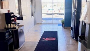 A hotel lobby with a reception desk, a coffee machine, a refrigerator, and a large window with a view of parked cars outside. - Motel 6 Grants, NM (Grants)