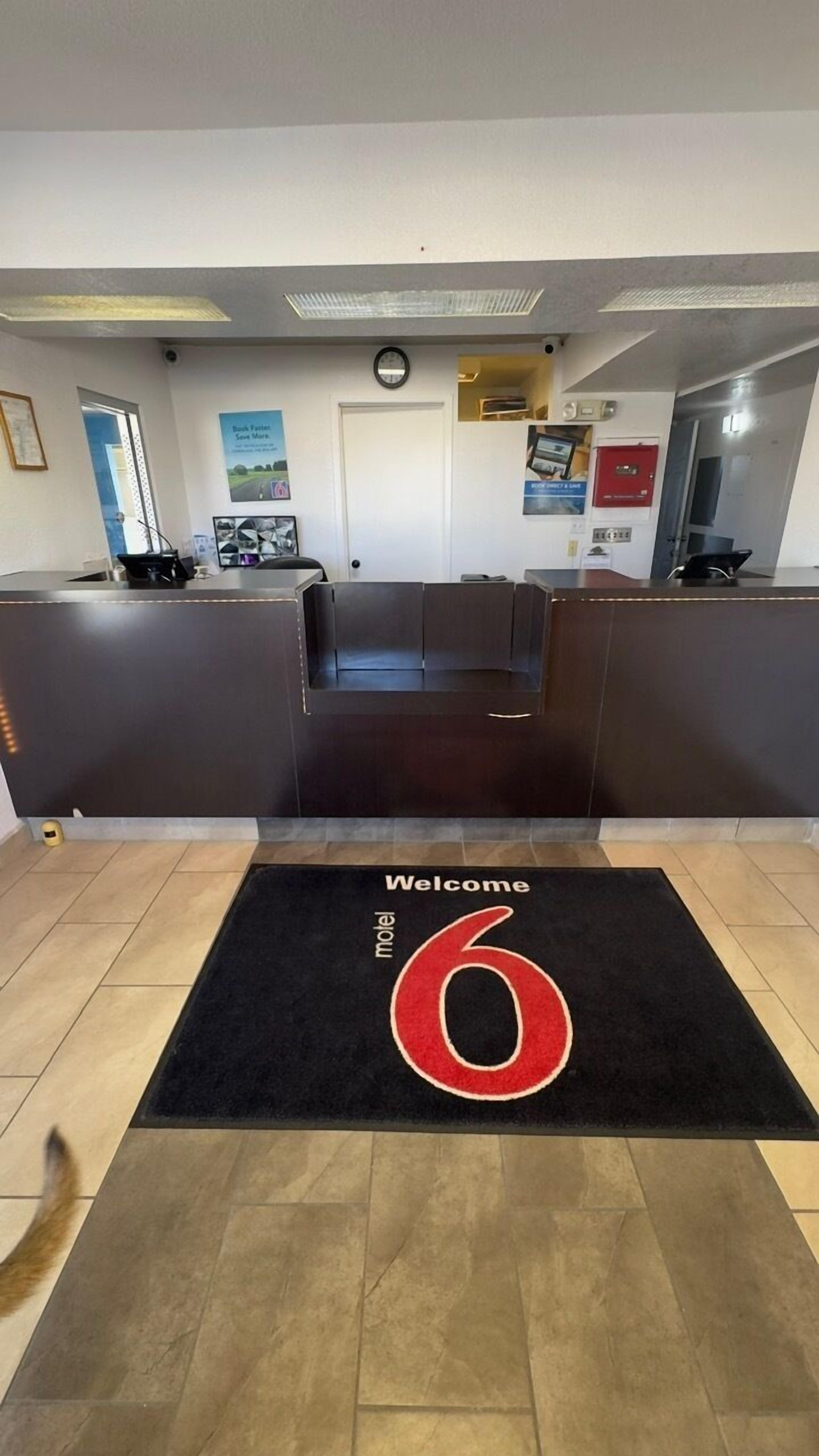 Un área de recepción con alfombra negra que muestra el número '6' en rojo y las palabras 'Welcome' y 'motel'.