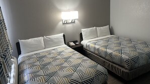 A hotel room with two beds, each with patterned bedding, a nightstand with a phone, and a wall-mounted light fixture. - Motel 6 Grants, NM (Grants)