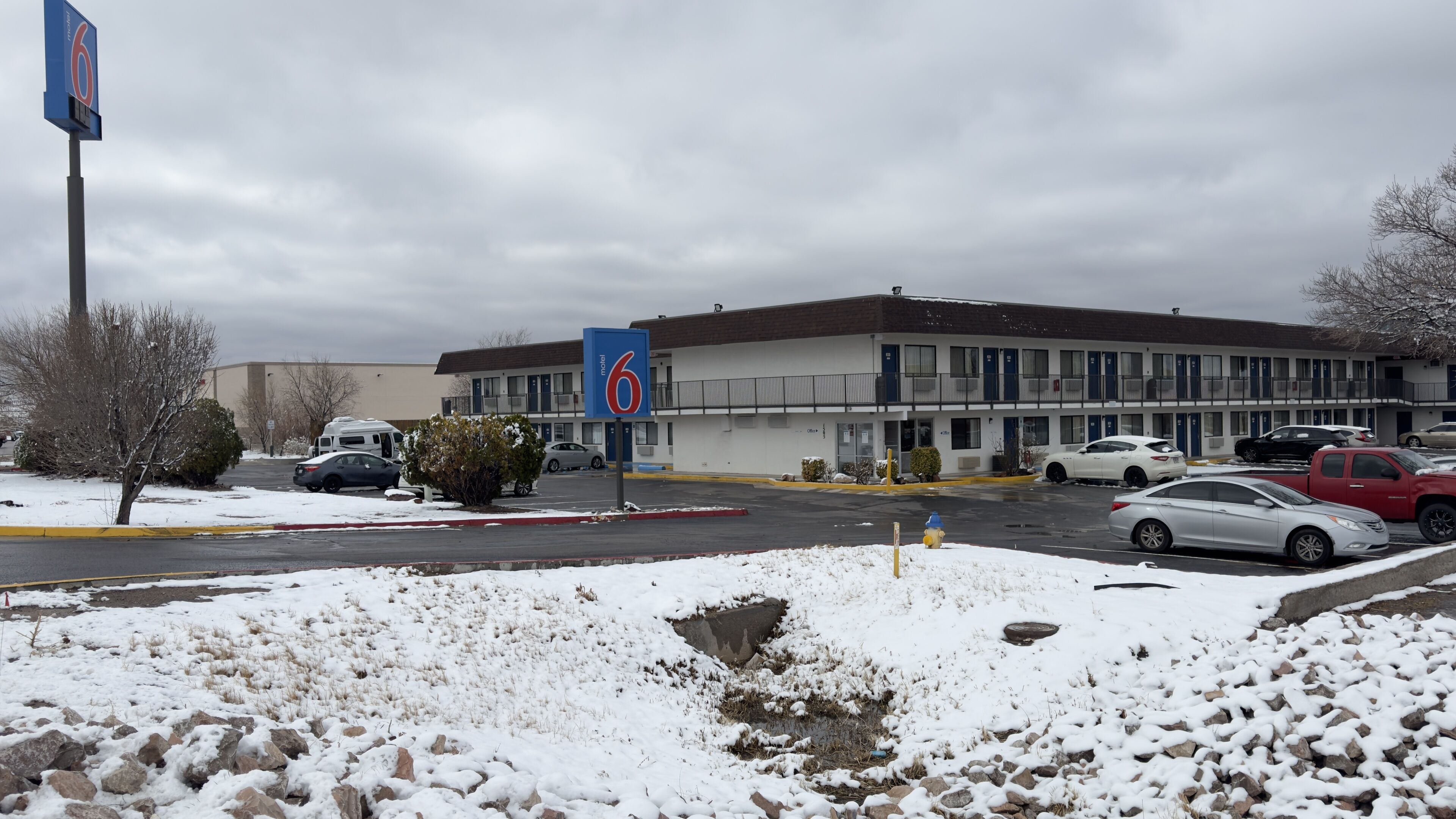 A motel with a parking lot, snow-covered ground, and a building with multiple windows and balconies.