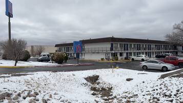 A motel with a parking lot, snow-covered ground, and a building with multiple windows and balconies.