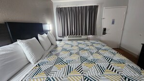 Habitación de hotel con cama, cabecera, ventana con cortinas, unidad de aire acondicionado y puerta con cerradura.