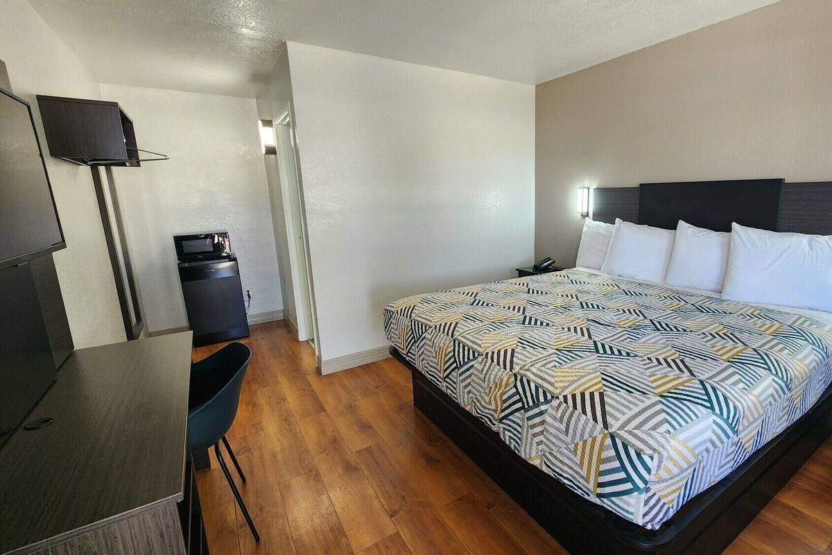 A hotel room with a bed, bedside table, desk, and a TV mounted on the wall.
