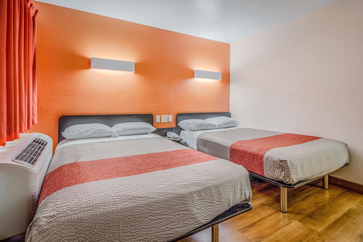 A hotel room with two beds, a heater, and a window with curtains.