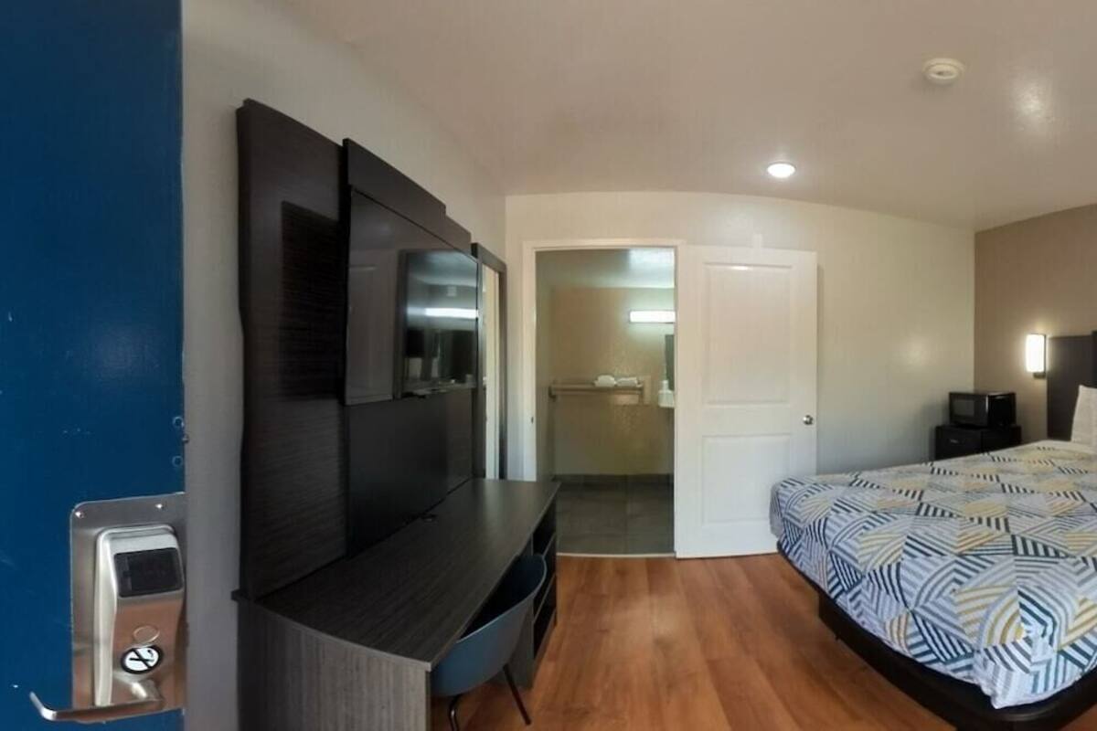A bedroom with a bed, bedside tables, a TV, a heater, and a window with curtains.