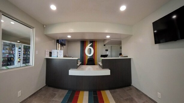 Un área de recepción con un mostrador curvo, un gran número '6' en la pared, máquinas expendedoras y un televisor de pantalla plana montado en la pared.