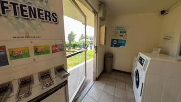 Una lavandería con lavadoras y secadoras de monedas, un letrero que dice 'EASIER LAUNDRY' y vista al exterior.